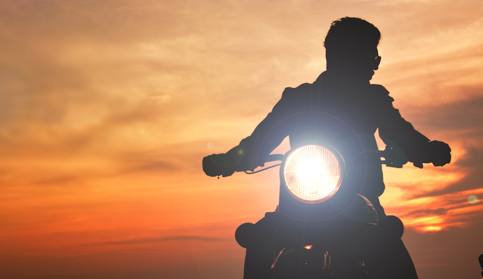 Motorcycle rider silhouetted against the sunset with the headlight on